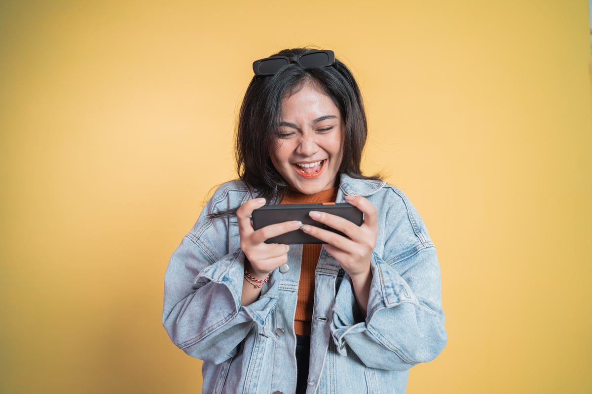 Asian Girl Laughing While Playing Game Using Cell Phone